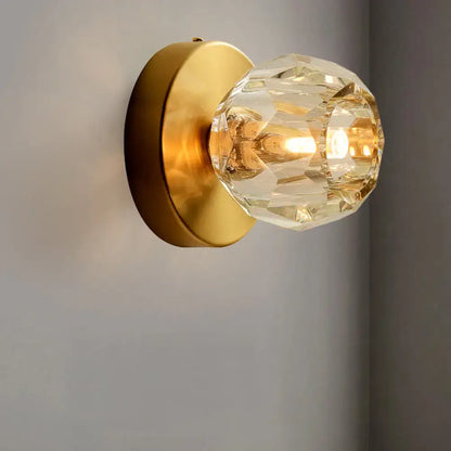 Contemporary golden wall mount lamp with faceted glass shade and brushed brass backplate for living room use