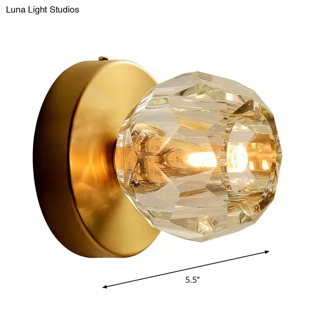 Contemporary golden wall mount lamp with faceted glass shade and warm glow on brushed brass for living room use