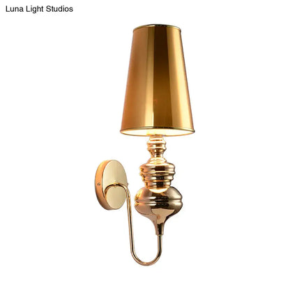 Gold-finished brass wall mount light with tapered reflective lampshade and ornate curved arm for bedroom use