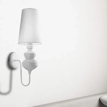 White ceramic wall mount light with a tapered fabric lampshade and curved arm for contemporary bedroom use