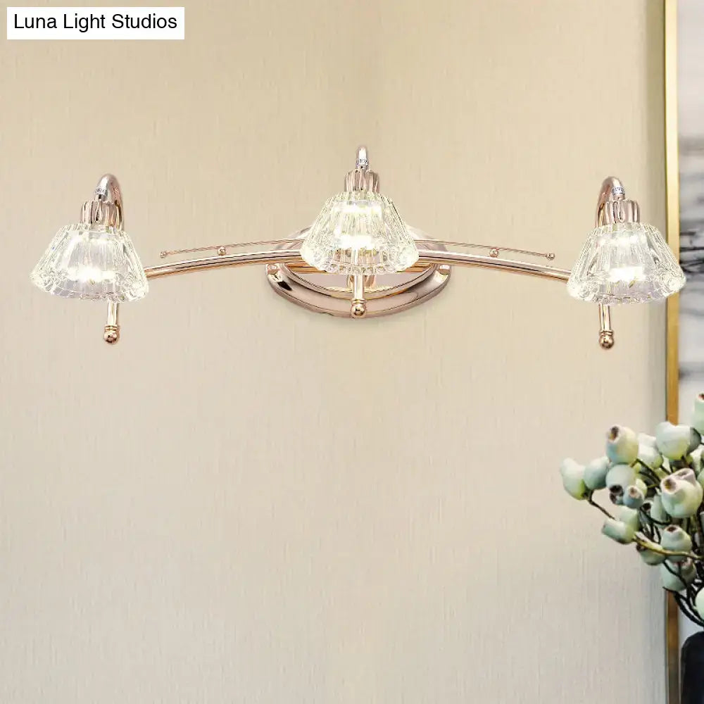 A sleek rose gold wall vanity light with three polished brass lights and faceted truncated cone crystal shades