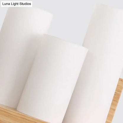 Contemporary tube shade wall lamp with wooden shelf featuring three white cylindrical matte candles on wooden surface