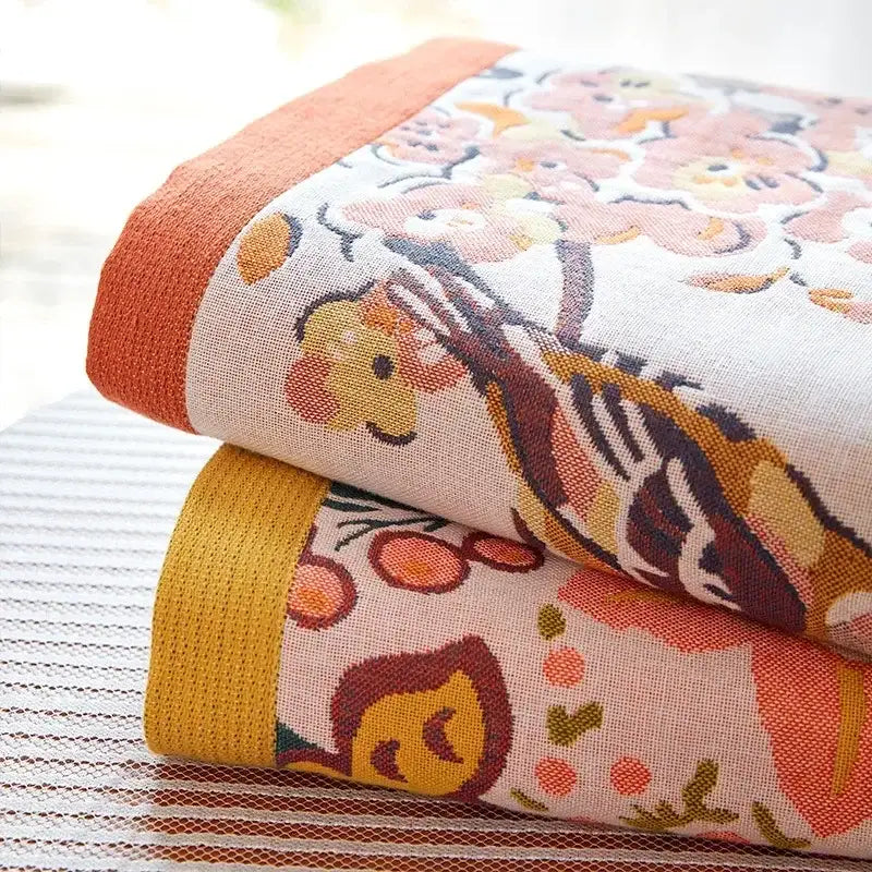 Stacked cotton gauze peacock cream and orange bath towels with soft floral pattern in warm peach and mustard tones