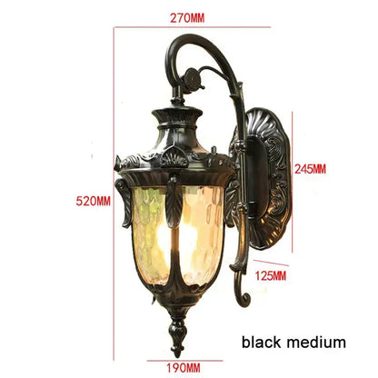 Country black wrought iron outdoor wall lantern with textured amber glass shade and ornate scrollwork detailing
