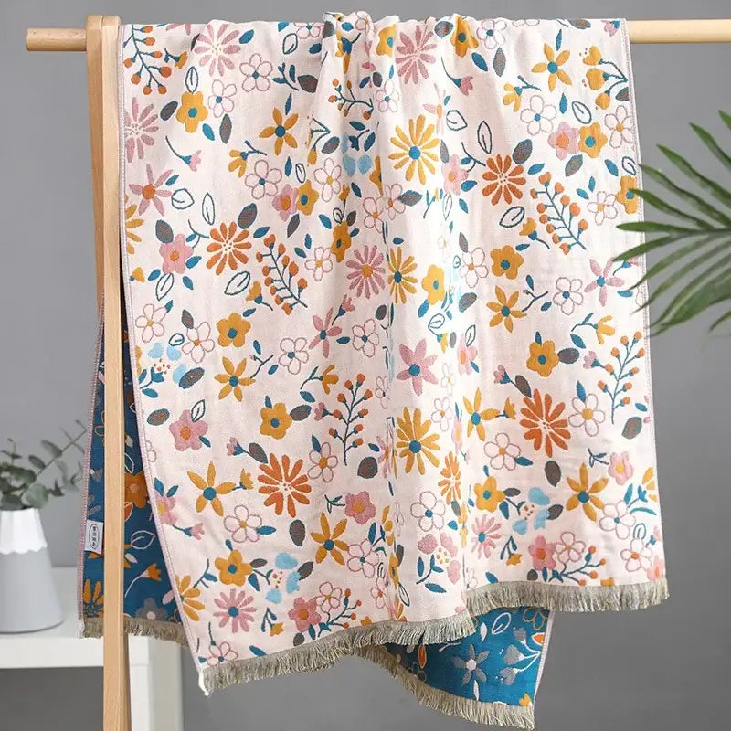 A cream-colored country flowers cotton floral knit throw blanket with vibrant orange pink yellow blue pattern and fringed edges