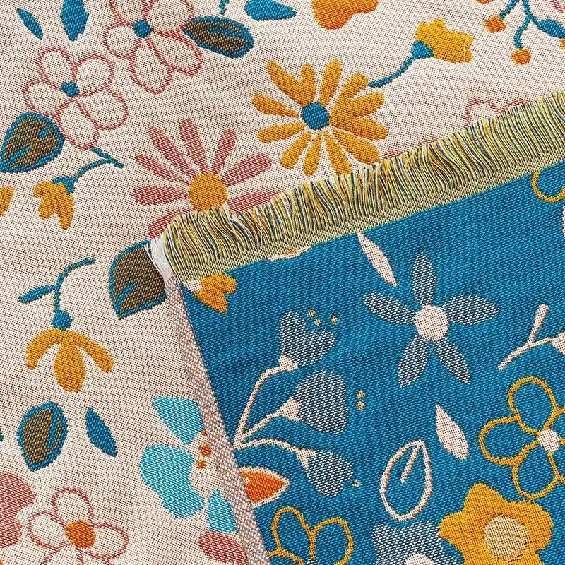 A country flowers cotton knit throw blanket with vibrant blue yellow pink floral pattern on off-white with fringed edges decorbites