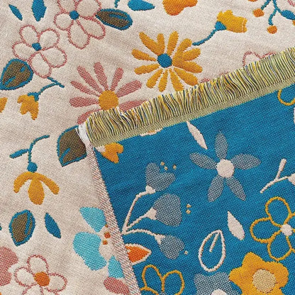 A country flowers cotton knit throw blanket with vibrant blue yellow pink floral pattern on off-white with fringed edges decorbites