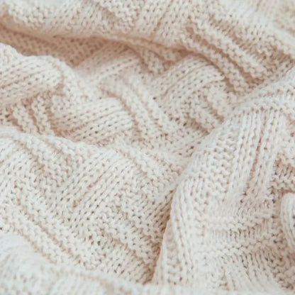 Cream-colored cable-knit sweater with soft textured weave paired with decorbites cozy fringed plaid throw blanket