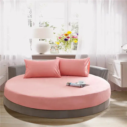 Pink circular bed with gray base and matching pink pillows featuring a cream and gray round fitted bed sheet set