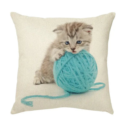 Beige linen throw pillow with cute cat face featuring a fluffy tabby kitten and bright teal yarn ball design