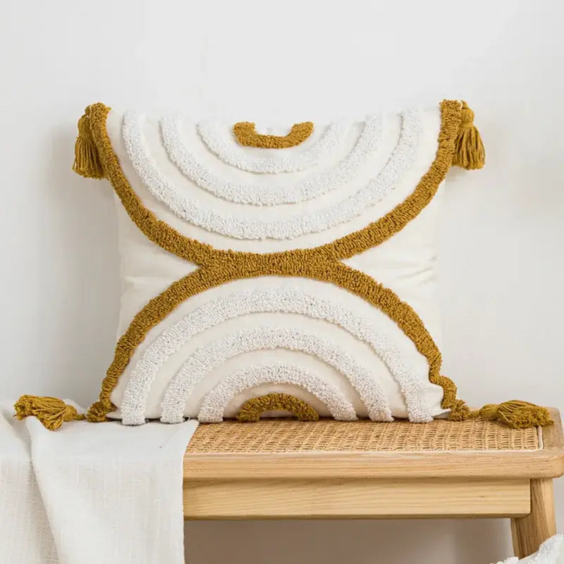 Cream cushion cover with geometric embroidery featuring textured layered rainbow patterns in mustard yellow and white yarn with tassels by Decorbites