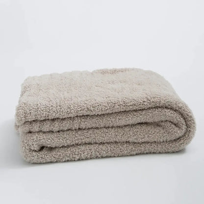 A cream knitted throw blanket with ribbed plush microfiber and a soft beige terry cloth bath towel surface