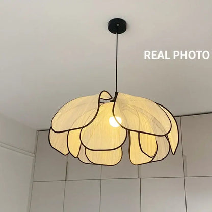 A warm-toned pendant light with layered petal shapes made of creamy abaca fabric and dark woven outlines by decorbites