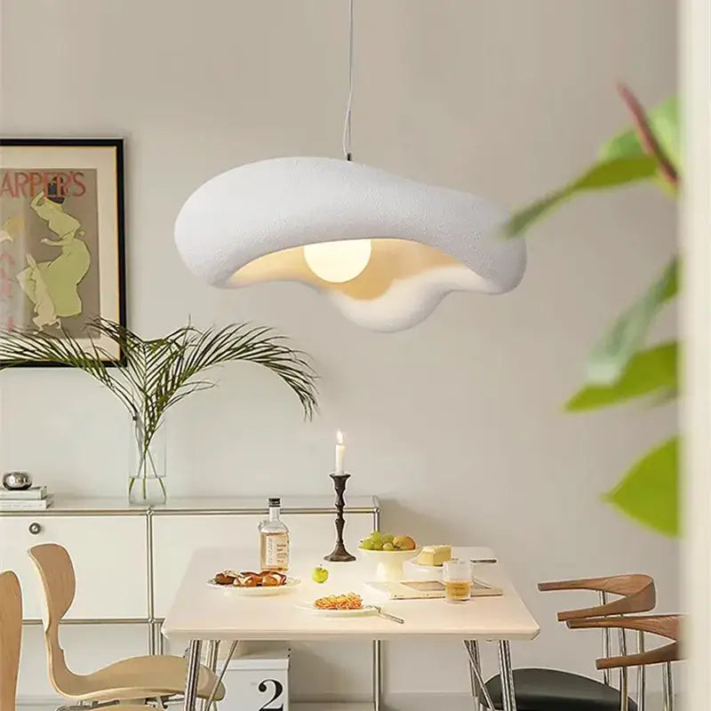 A modern creamy style resin white pendant light with a cloud-like textured surface hangs above a dining table
