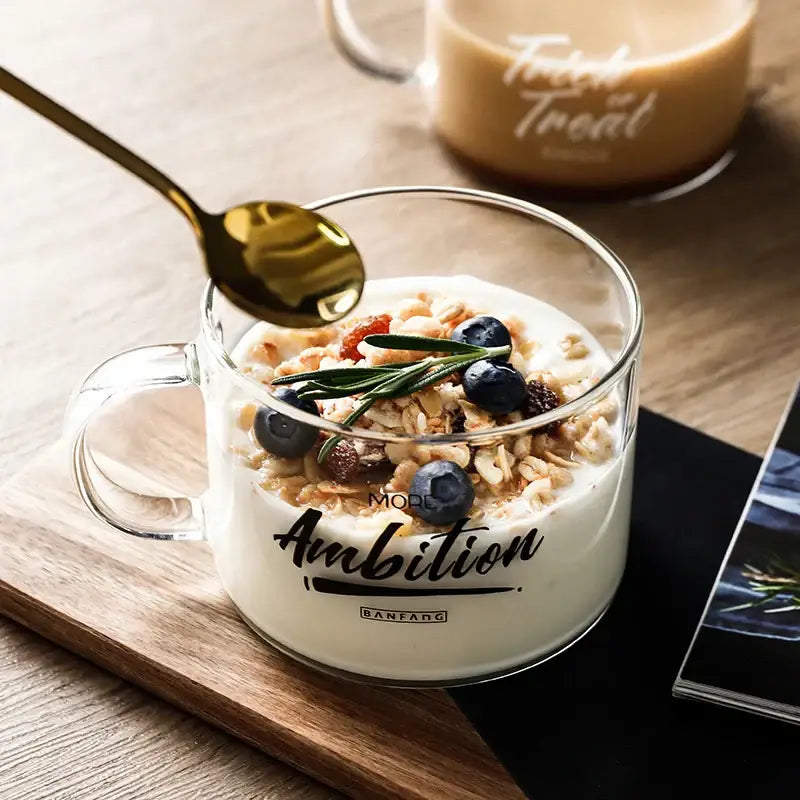 Clear glass creative alphabet glass mug with ambition cursive print filled with yogurt granola blueberries and rosemary