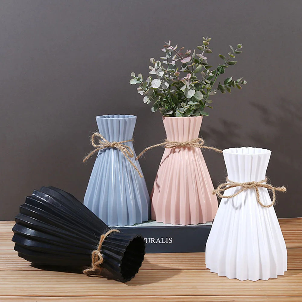 Three pleated European style flower bottles in blue, blush pink, and white plastic tied with twine at the waist