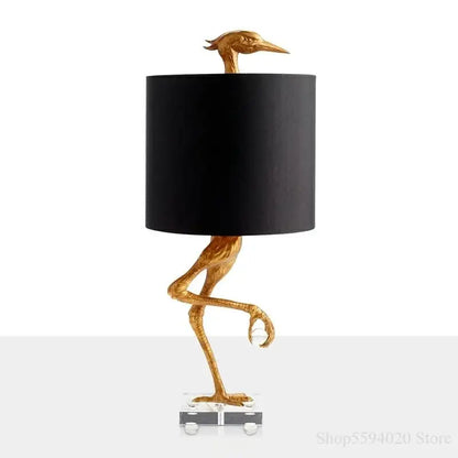 Golden bird-shaped creative ostrich table lamp with black cylindrical shade and clear acrylic base for bedroom decorbites