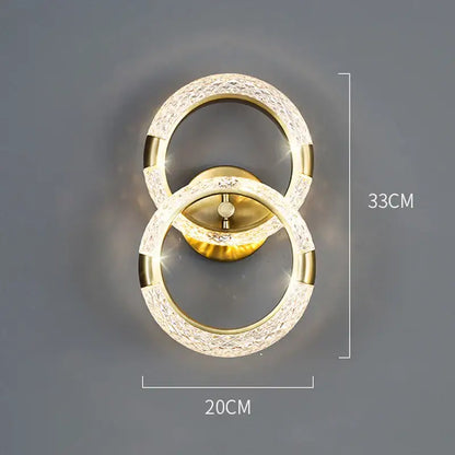 Gold-toned decorbites crystal nordic wall sconce with two interlocking rings and sparkling crystal accents for bedroom light