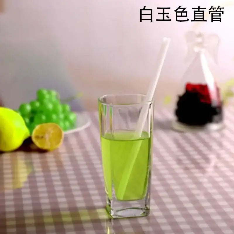 A clear glass tumbler with vibrant green liquid and a curved amber glass drinking straw kitchen accessory