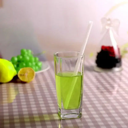 A curved amber glass drinking straw in a clear tumbler with vibrant green liquid and a white glass drinking straw