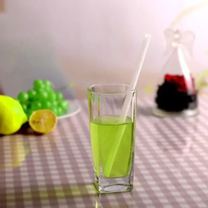 A curved amber glass drinking straw in a clear tumbler with vibrant green liquid and a white glass drinking straw