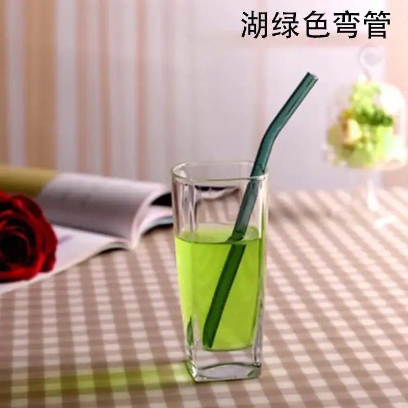 A sleek curved amber glass drinking straw in vibrant lake green liquid inside a clear drinking glass for glass drinking