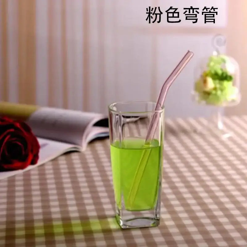 A translucent pink curved glass drinking straw in a clear glass with vibrant green liquid for stylish drinking use