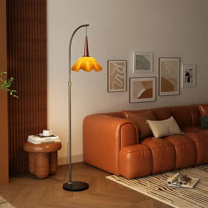 Curved black floor lamp with polished metal frame and amber fabric shade beside a living room shelf for living room floor use