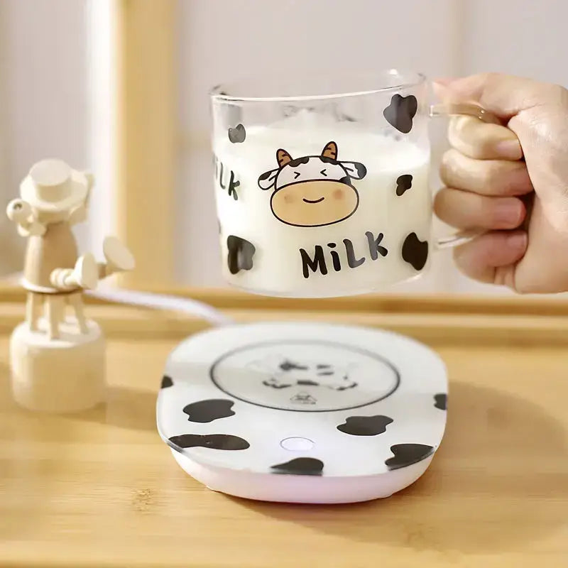 Cute cartoon cow pattern glass mug with spoon lid and black spots held above matching spotted heating pad in dining room