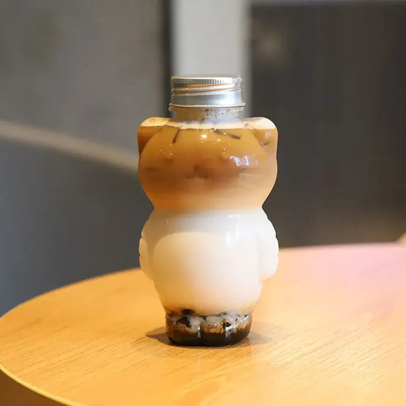 Clear plastic bear-shaped cute cat beverage bottle with silver cap filled with layered iced coffee and tapioca pearls
