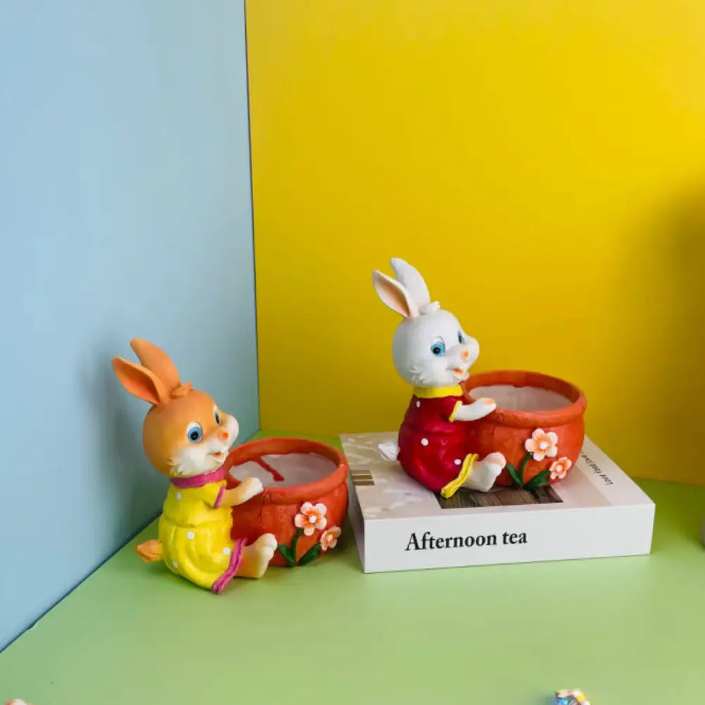 Two ceramic bunny rabbit flower pots in yellow and red holding orange pots decorated with pink flowers garden decor