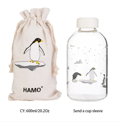 Clear glass decorbites blue glass water bottle with white cap and penguin design with matching beige drawstring bag