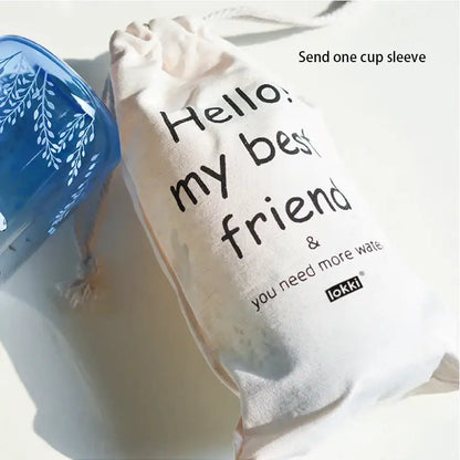 Cream-colored drawstring bag with black text and lokki logo paired with cute polar bear and seal decorbites blue glass water bottle