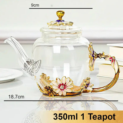 A clear crystal glass teapot set with gold-toned floral embellishments and ornate handle for dining room use