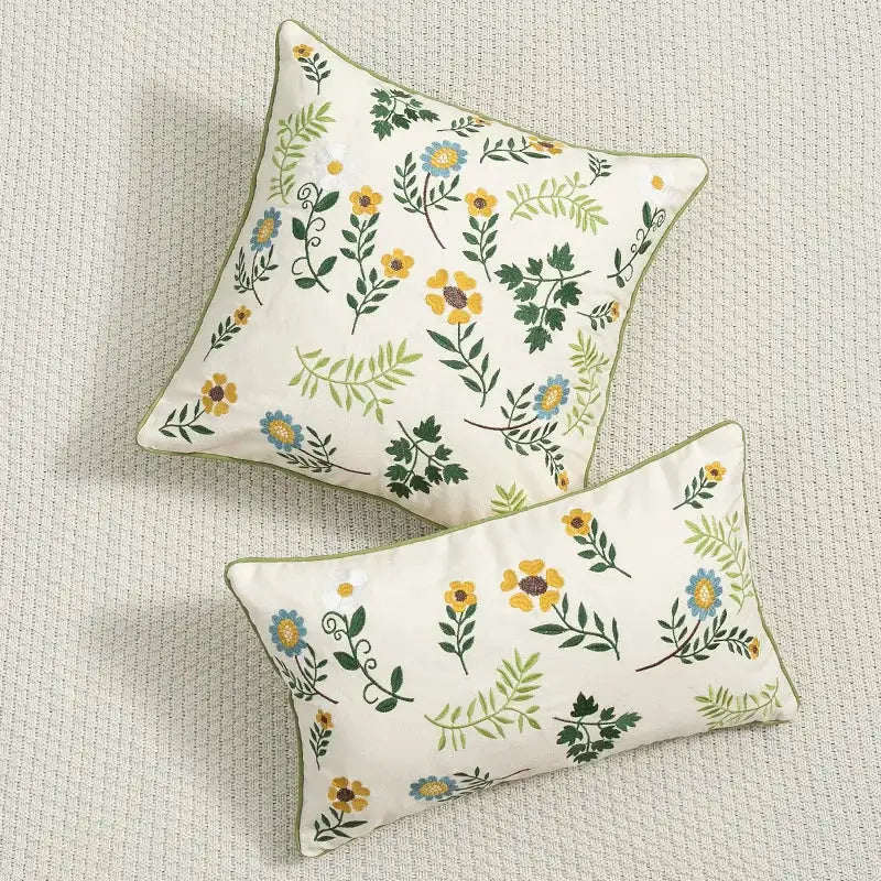 Cream-colored cushion cover with daisy floral embroidery in yellow blue and green hues and olive-green piping by decorbites