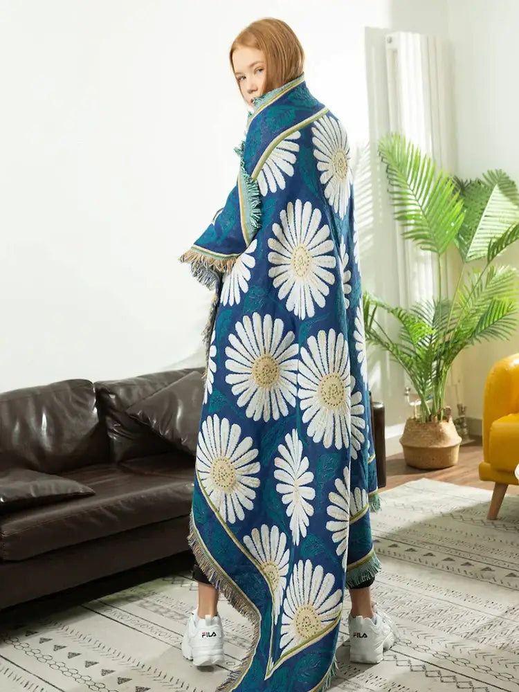 A vibrant blue daisy flower knitted blanket with bold white daisies and gold accents draped over shoulders