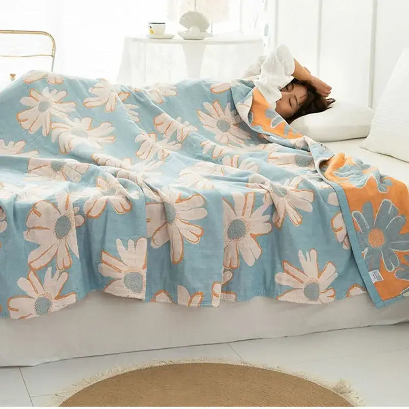 A soft light blue double cotton blanket with a cheerful white and orange daisy pattern for bedroom use