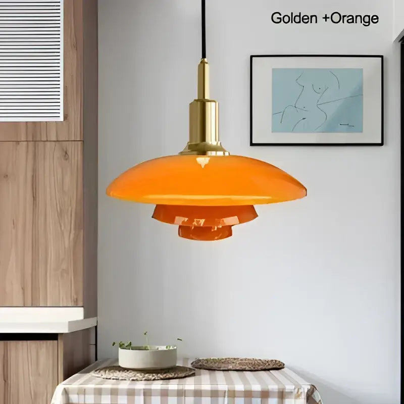 Orange glass pendant light with frosted tiered design and golden brass fixture as a dining room focal point