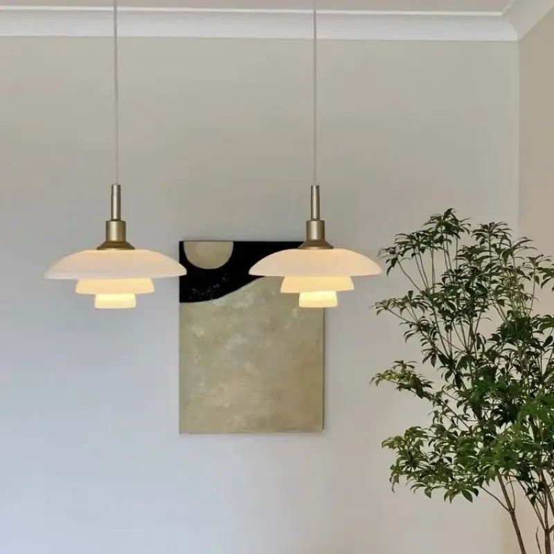 Two elegant Danish tiered frosted glass pendant lights with brass fixtures create a warm focal point for dining rooms