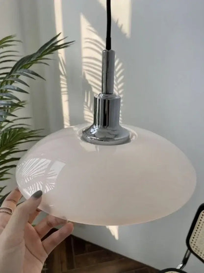 A sleek off-white glass pendant light with polished chrome fixture serves as a focal point in dining room decor