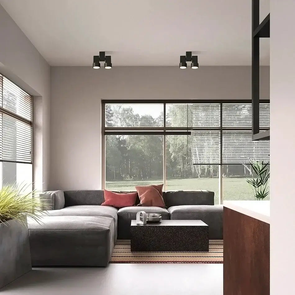 Modern white surface mount downlight installed above a gray sectional sofa with plush cushions and reddish-pink pillows