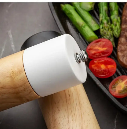 A sleek white ceramic manual wooden salt pepper grinder with natural wood handle resting beside grilled vegetables