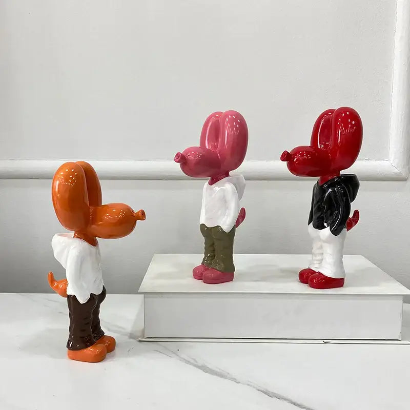 Three glossy orange pink and red resin balloon dog statues by decorbites with white shirts and distinct pants for home decor