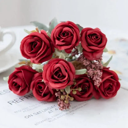 A bouquet of vibrant red artificial roses with green leaves and pink embellishments in a pink peony silk bouquet design