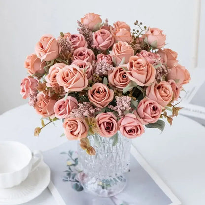 A peony silk bouquet of soft peach-colored roses and delicate greenery in a clear faceted crystal vase for decoration