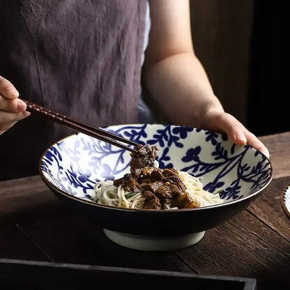 A ceramic japanese ramen bowl with black exterior and blue floral interior filled with noodles and meat soup
