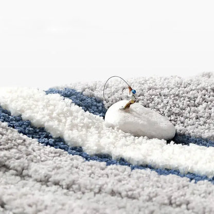 A miniature fishing figurine on a smooth white stone on a soft blue and white striped decorbites absorbent water bathroom mat