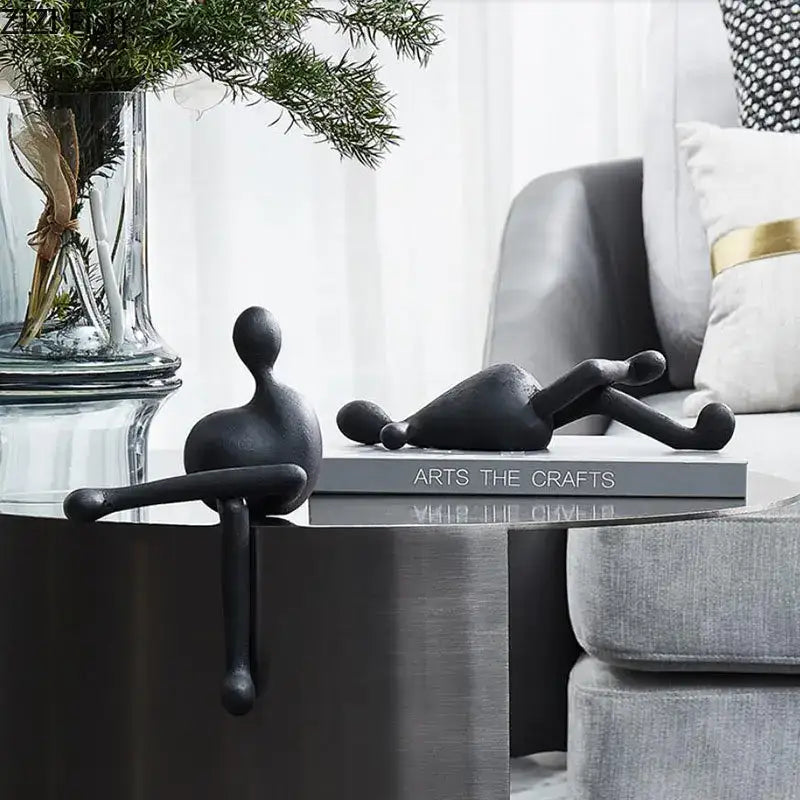 Two black minimalist abstract characters resin figurines by decorbites rest on books on a modern metallic table