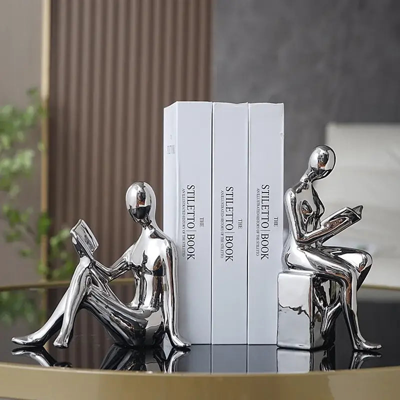 Shiny silver metallic decorbites abstract figure bookend set featuring two seated figures reading books for stylish decor