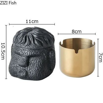 Black textured skull-shaped portraits cement ashtray with gold-toned cylindrical base and four notches for smoking accessories